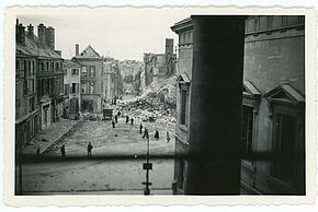 Photo en noir et blanc prise de l'intérieur d'un bâtiment depuis une fenêtre sur une place.